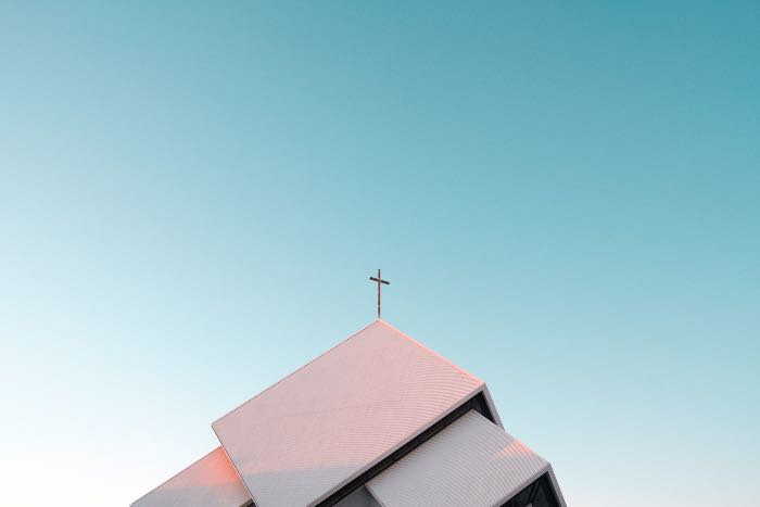 a photo of a church's roof, the sky, and in the center of the picture is the small cross at the top of the church.