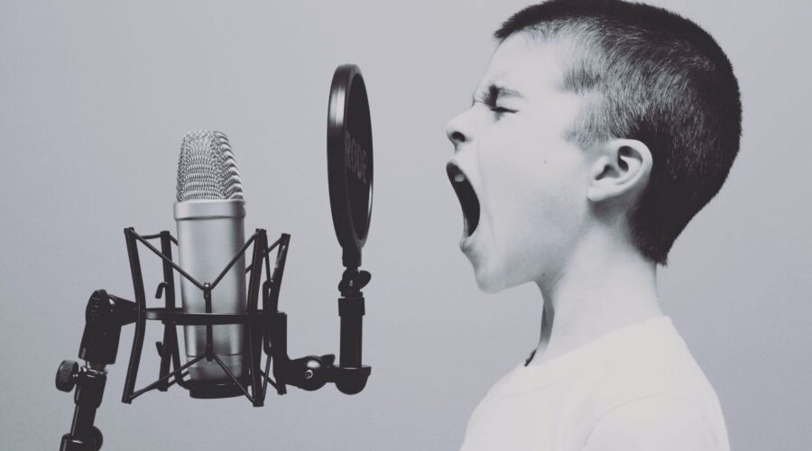 a photo of a boy who appears to be singing or shouting into a microphone (through a pop filter)
