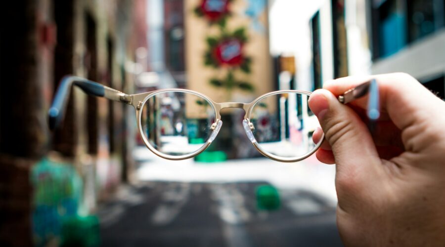 a photo of eyeglasses, held out, in the foreground, and the background is unfocused